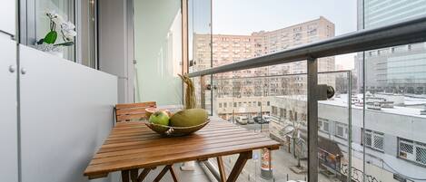 Un balcón con una mesa de madera, un cuenco de fruta y una planta en maceta.