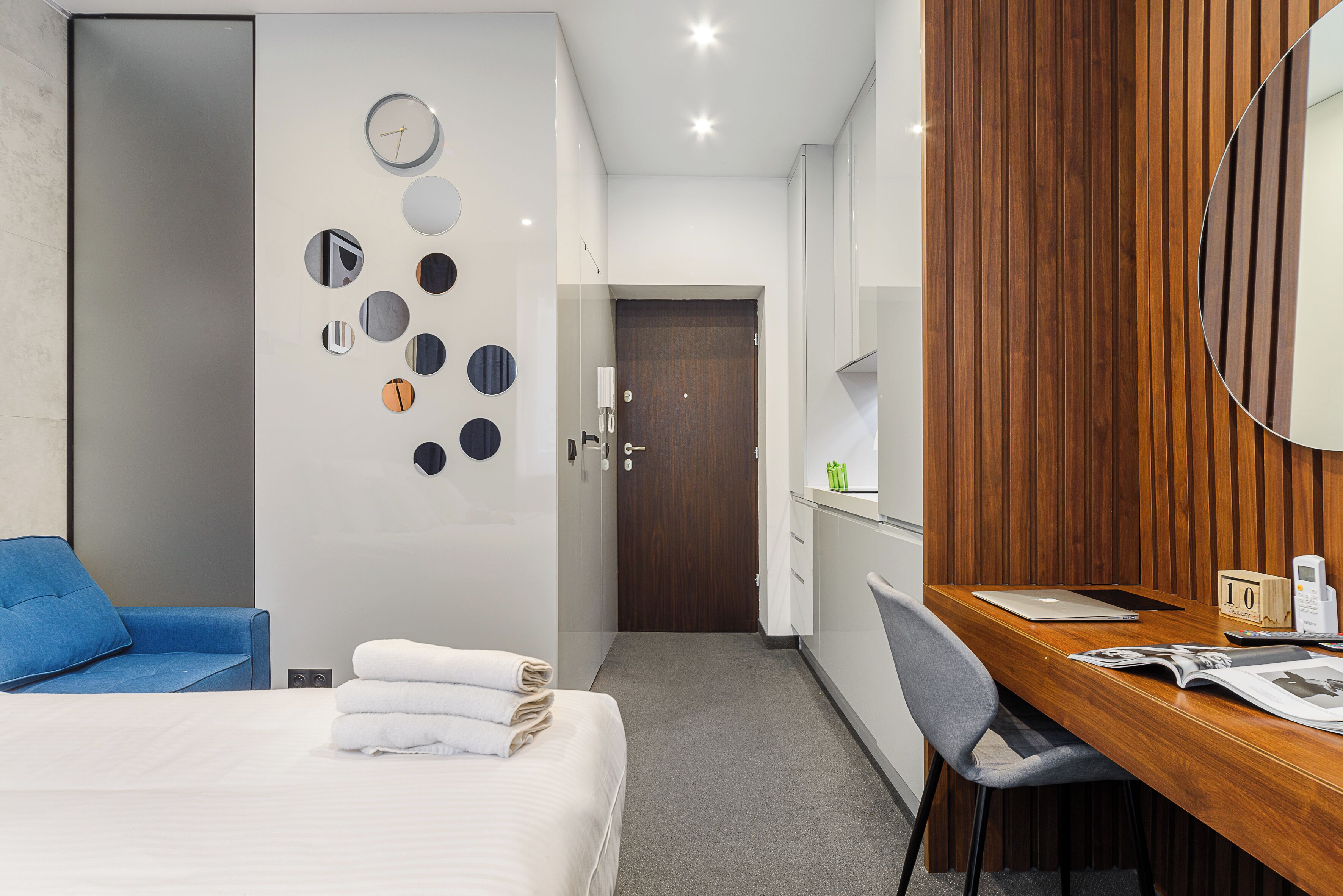 Een hotelkamer met een bed, een bureau met een laptop, een stoel, een blauwe bank en een wand van hout.