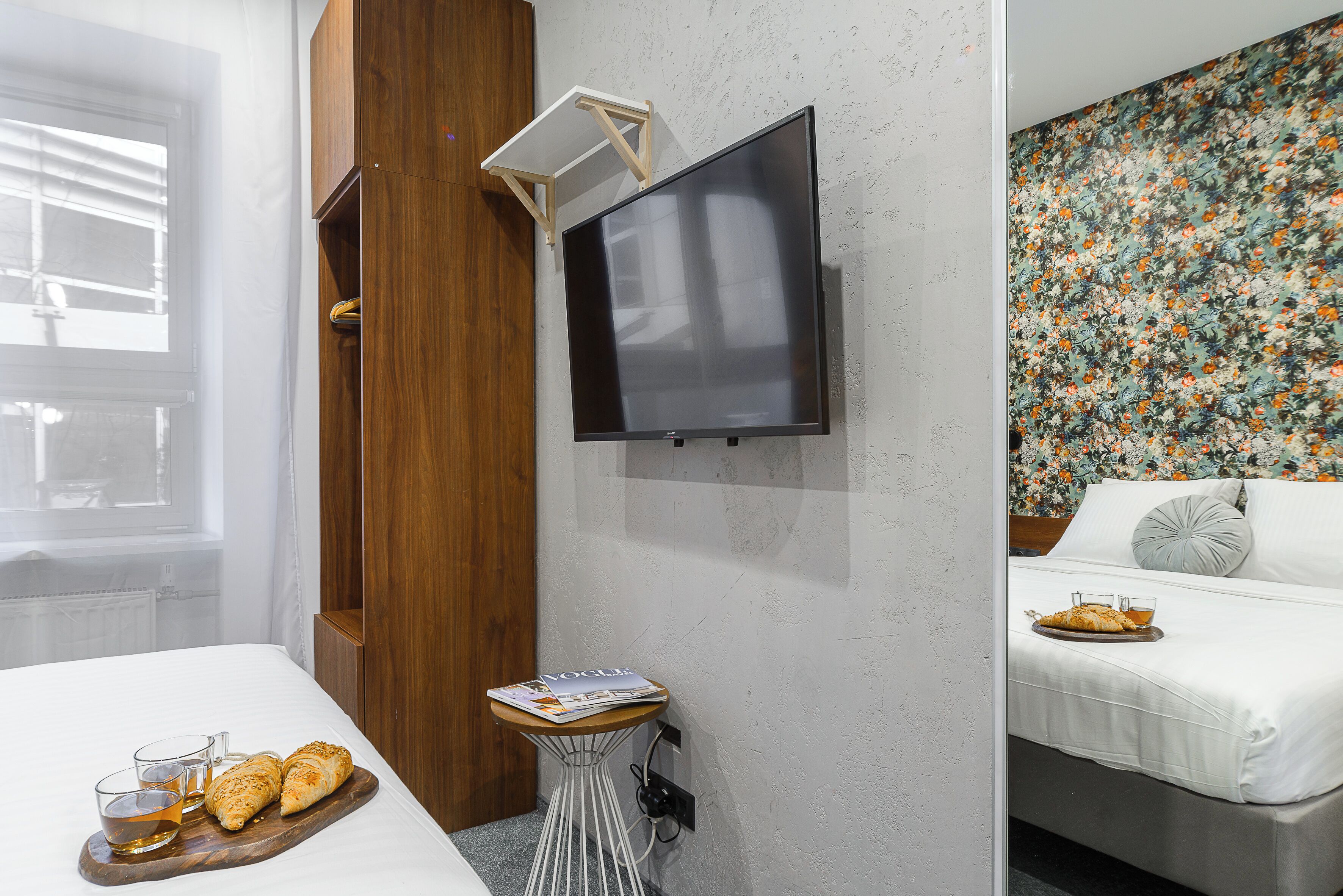 Une chambre d’hôtel avec un lit, une petite table sur laquelle se trouve un magazine, un plateau avec des croissants et un verre de jus de fruits, et un téléviseur fixé au mur.