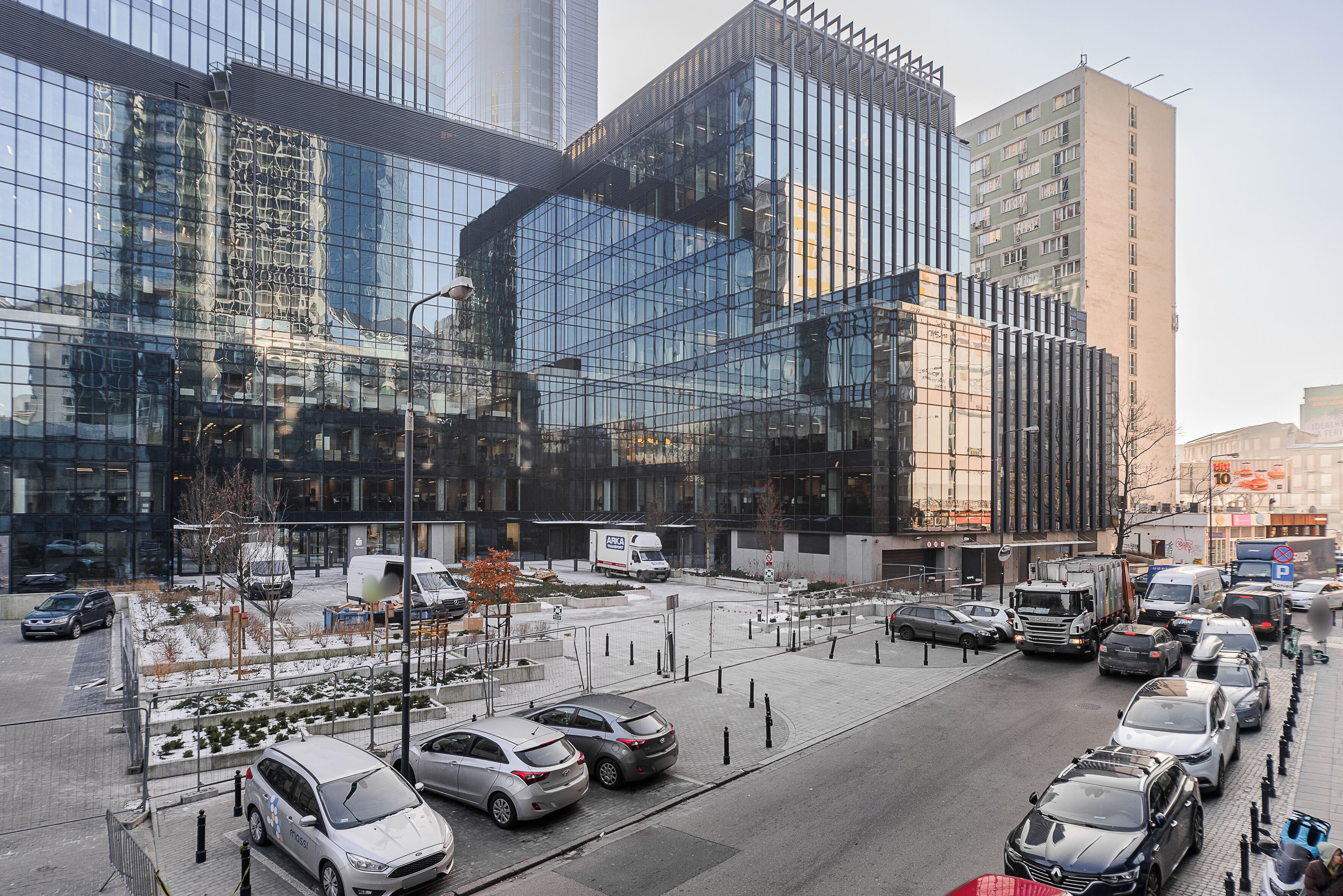 A modern urban street with high-rise buildings, parked cars, and a clear sky.