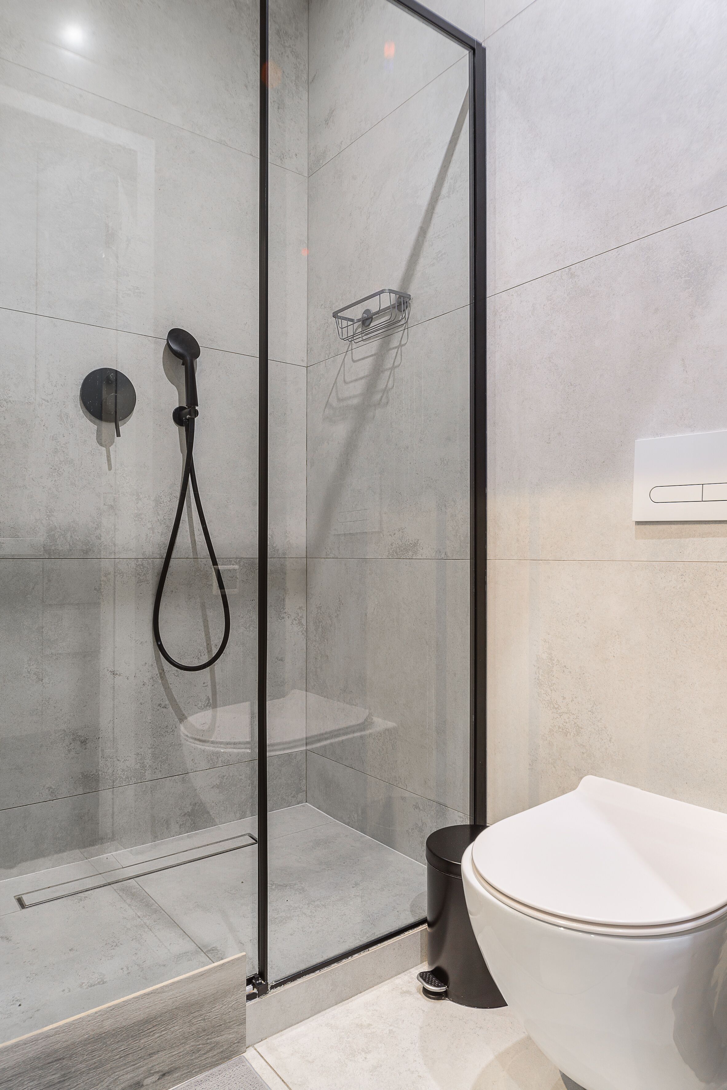 Un baño moderno con ducha envuelta en vidrio, inodoro blanco y un cubo de basura negro.