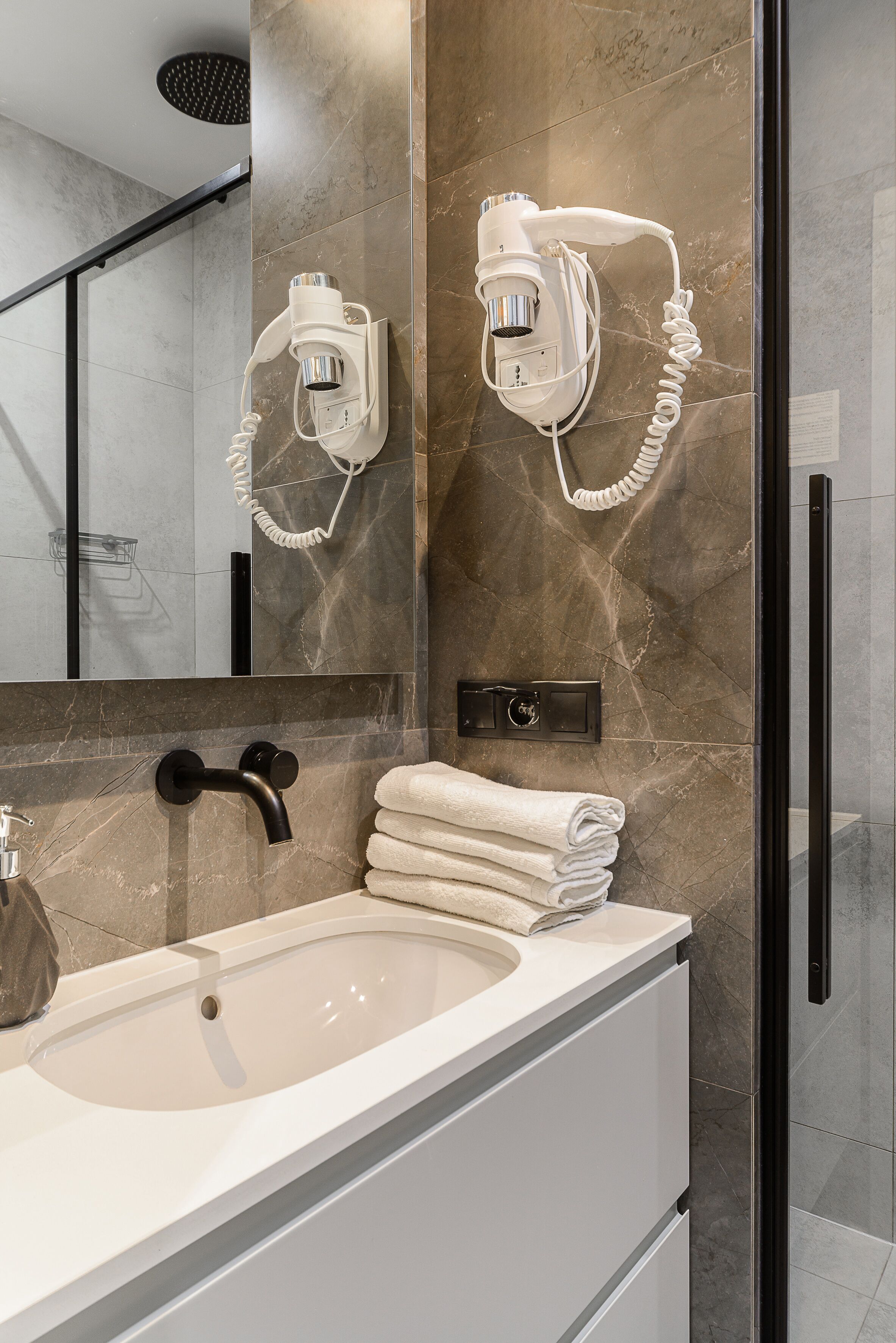 Un baño moderno con un espejo grande, un secador de pelo integrado, un grifo negro y una pila de toallas blancas.