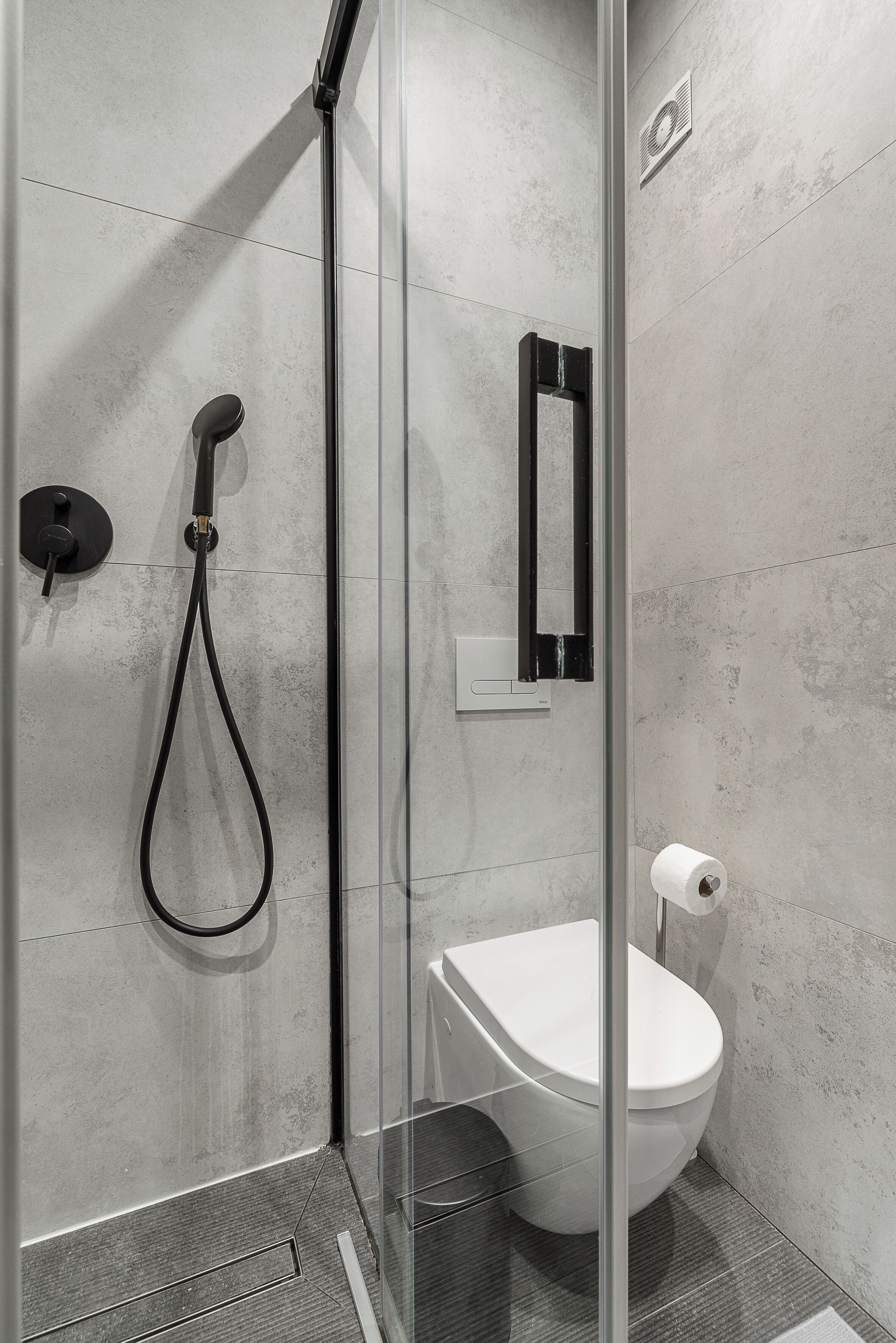 Une salle de bain moderne avec une douche à parois de verre, des toilettes blanches et un miroir fixé au mur.