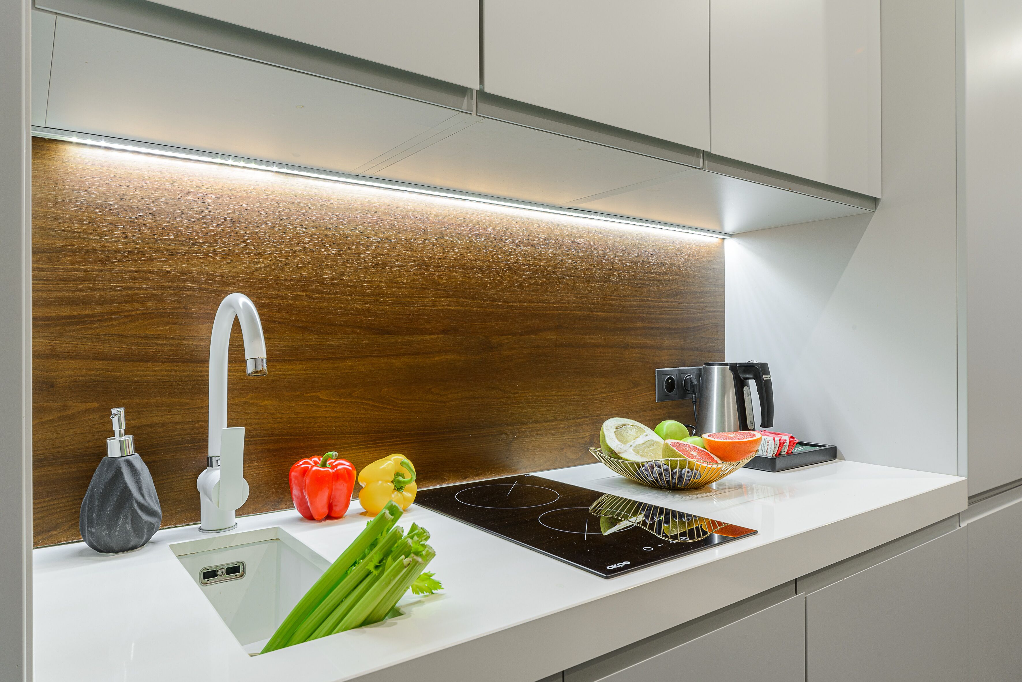 A modern kitchen with a built-in sink, a faucet, and a countertop with a cutting board, vegetables, and a kettle.