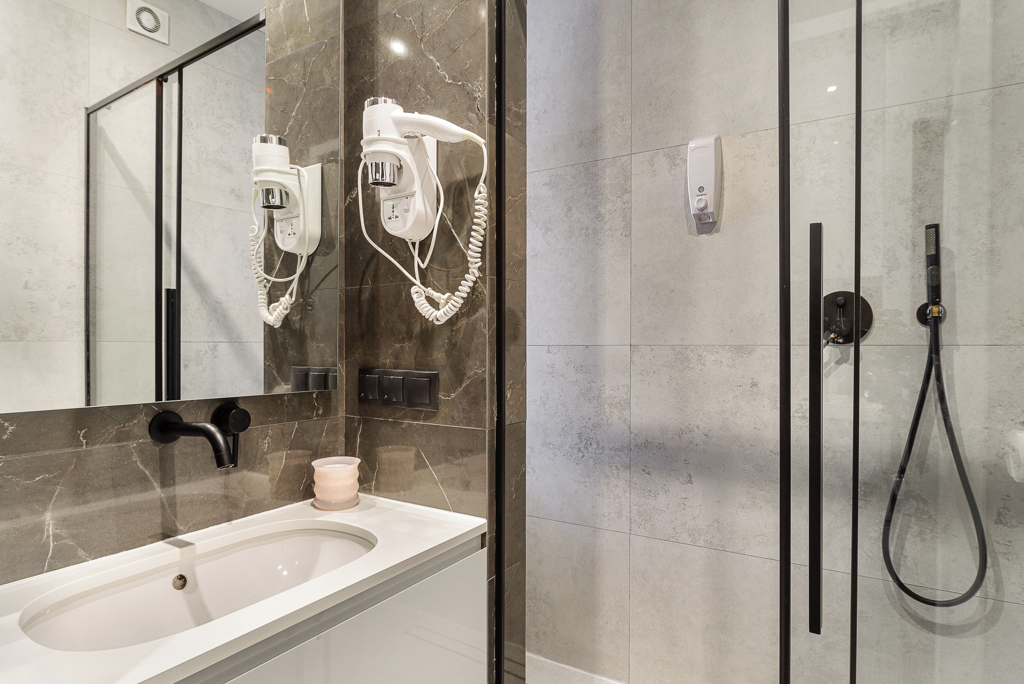 A modern bathroom with a large mirror, a hairdryer, a sink, and a shower area.