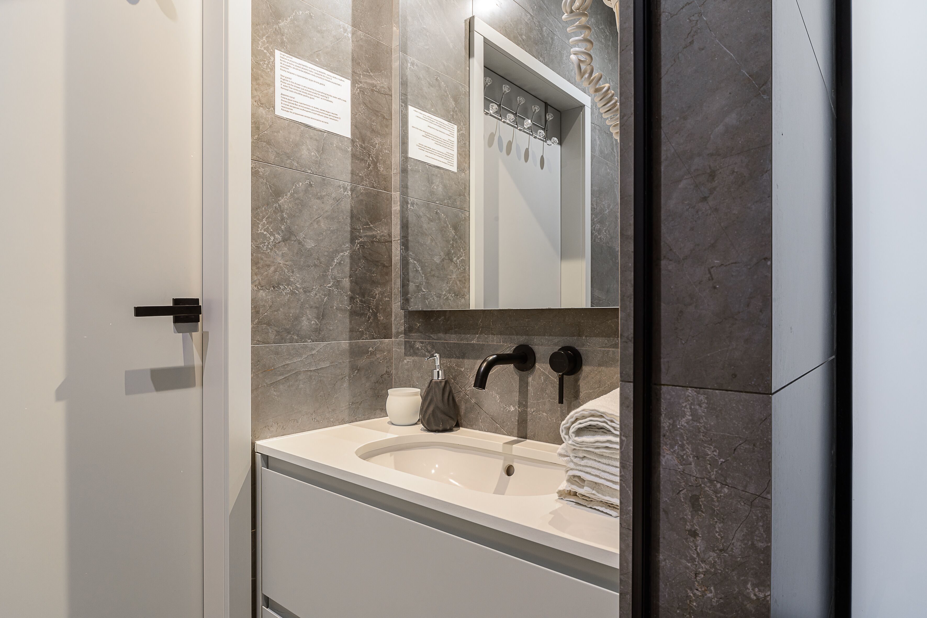 A modern bathroom with a marble wall, a sink, a mirror, and a towel rack.