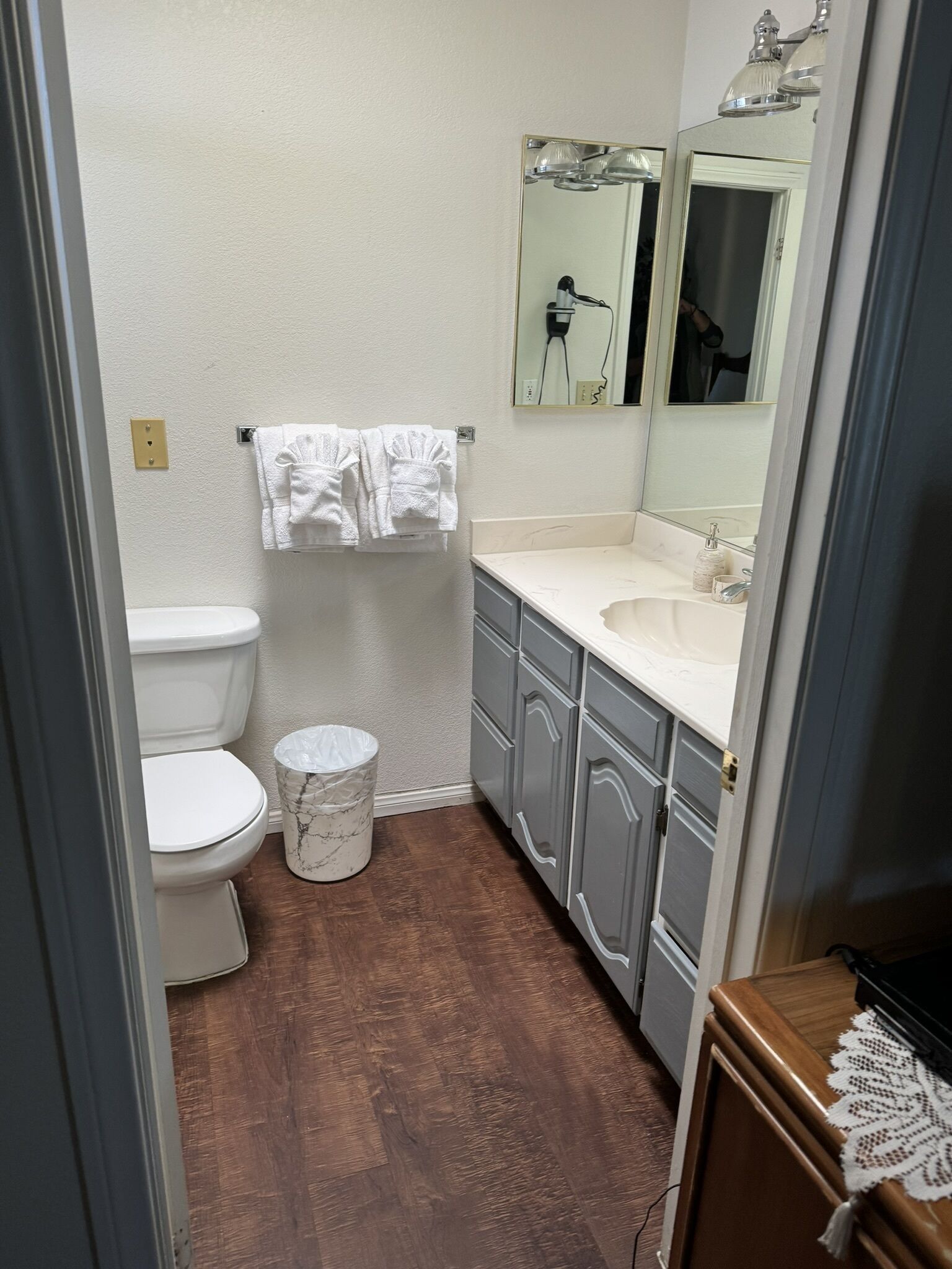 Ein kleines Badezimmer mit Toilette, Waschbecken und Spiegel. Handtücher hängen an der Wand und ein Mülleimer steht dort.