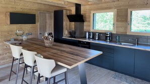 Una cocina moderna con paredes de madera, una isla central con taburetes de bar, una campana extractora negra y un ventanal con vistas a zonas verdes.