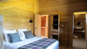 Un dormitorio de cabaña de madera con cama, mesita de noche, armario y baño con lavabo y espejo.