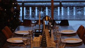 Una mesa de comedor lista para cuatro personas, con un centro decorativo, un árbol de Navidad y vistas a un paisaje nevado.