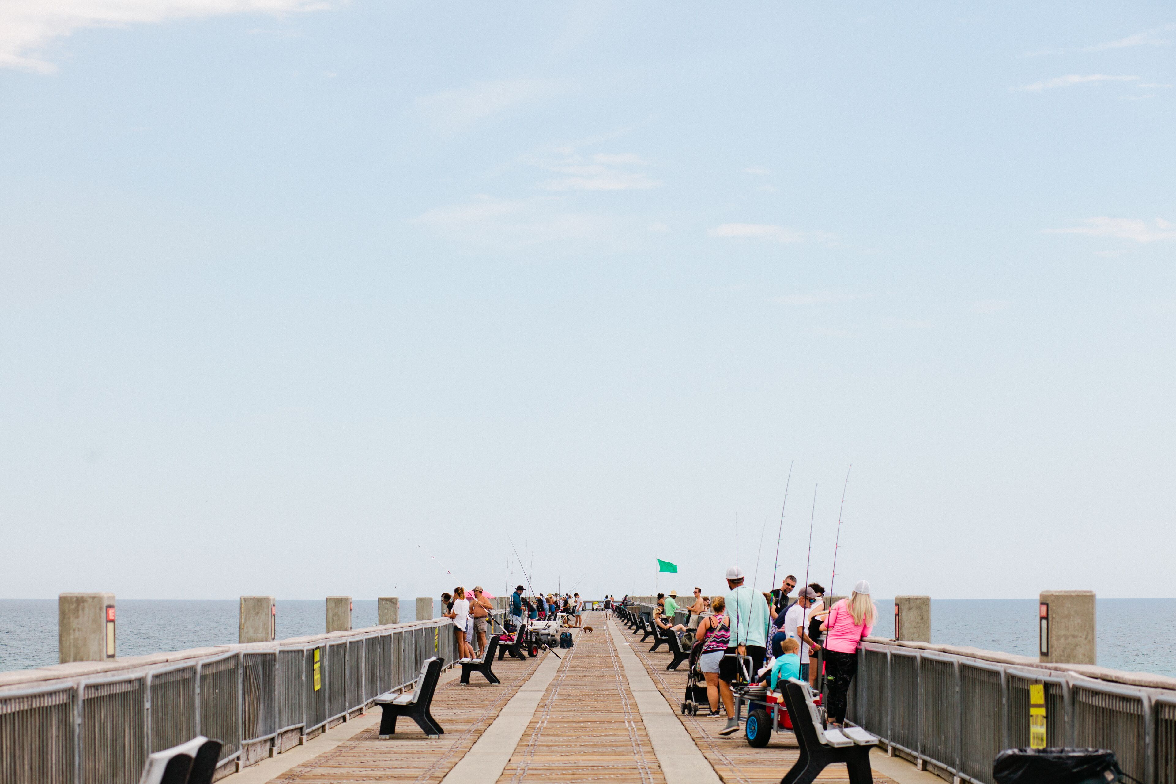 A pier with people fishing and sitting on benches, overlooking the water.