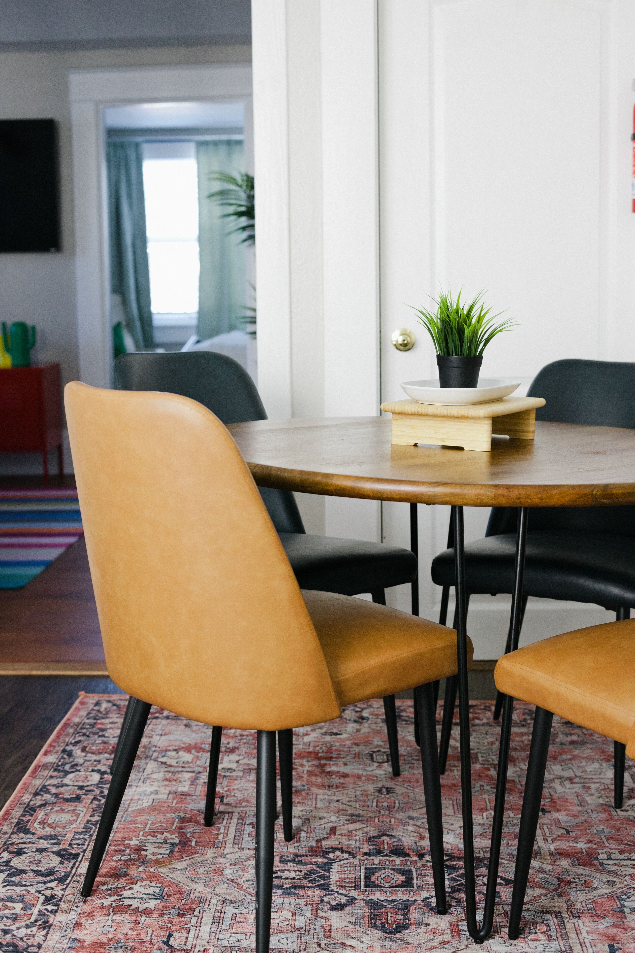 A dining area with a round wooden table, four chairs, a potted plant, and a patterned rug.