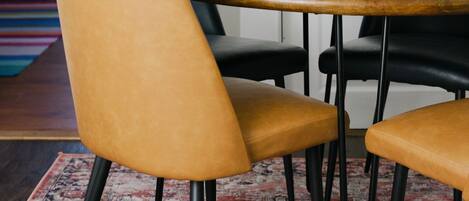 A dining area with a round wooden table, four chairs, a potted plant, and a patterned rug.
