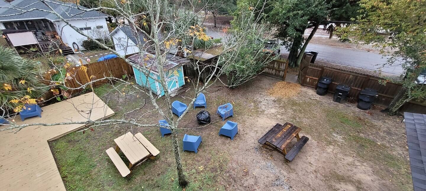 Patio trasero con terraza de madera, un árbol y sillas de plástico azul.