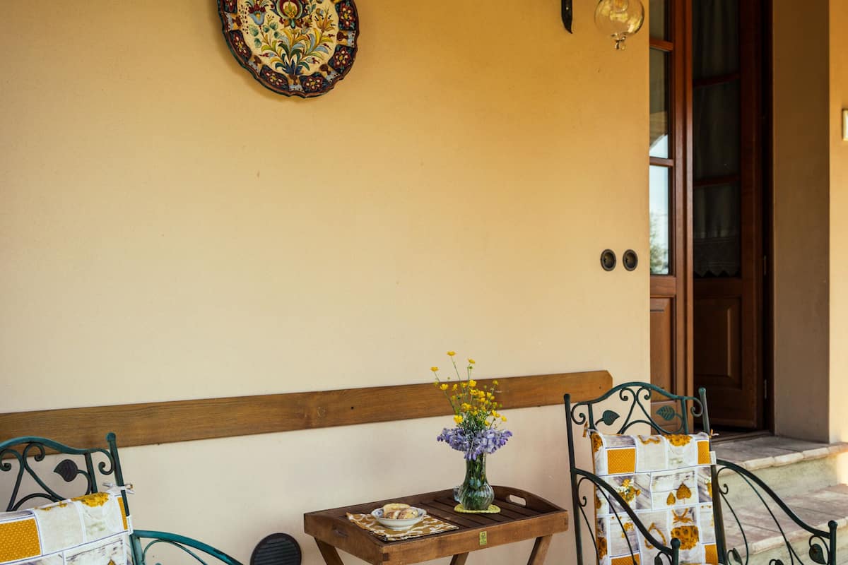 Un patio con dos sillas de metal, una mesita con un florero y un plato decorativo en la pared.