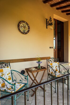 Eine Terrasse mit zwei Metallstühlen, einem kleinen Tisch mit einer Vase und einem dekorativen Teller an der Wand.