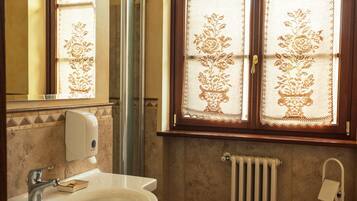 Ein Badezimmer mit weißem Waschbecken, einem Spiegel, einem Handtuchhalter, einem Fenster mit Spitzenvorhängen und einer Heizung.