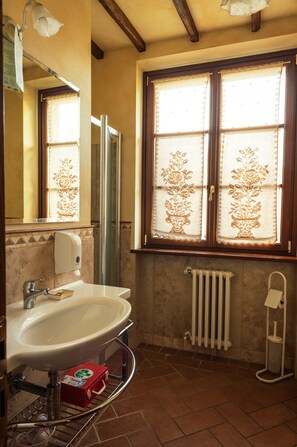 Ein Badezimmer mit weißem Waschbecken, einem Spiegel, einem Handtuchhalter, einem Fenster mit Spitzenvorhängen und einer Heizung.