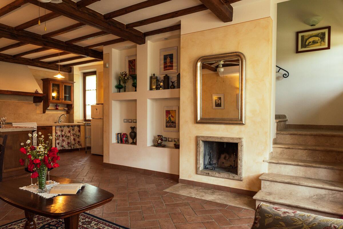 Amplia sala de estar con chimenea, vigas de madera y una escalera.