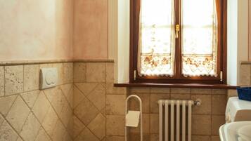 A bathroom with a bidet, a toilet, a sink, and a window with curtains.