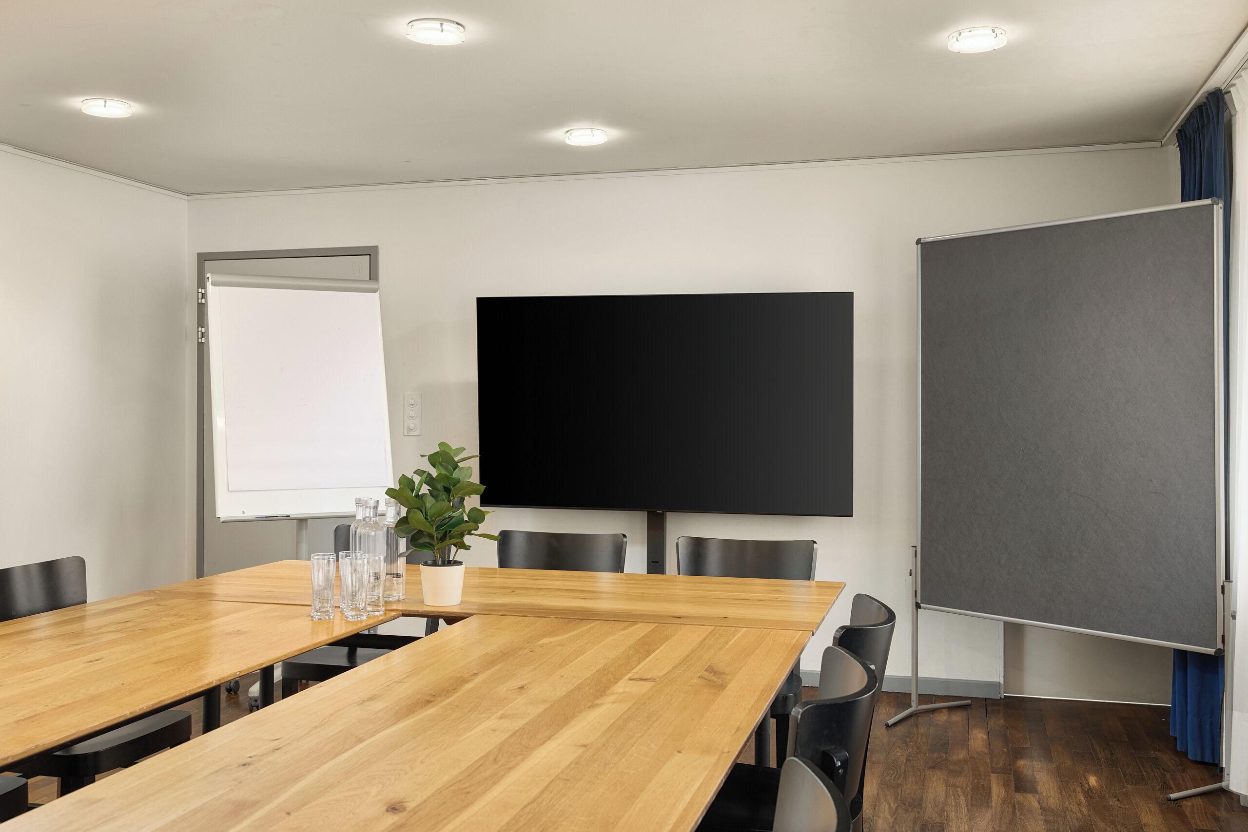 Una sala de conferencias con una larga mesa de madera, sillas, una pizarra, una pantalla de proyector y una planta en maceta.
