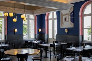 Interior de restaurante con mesas redondas, sillas e iluminación colgante.