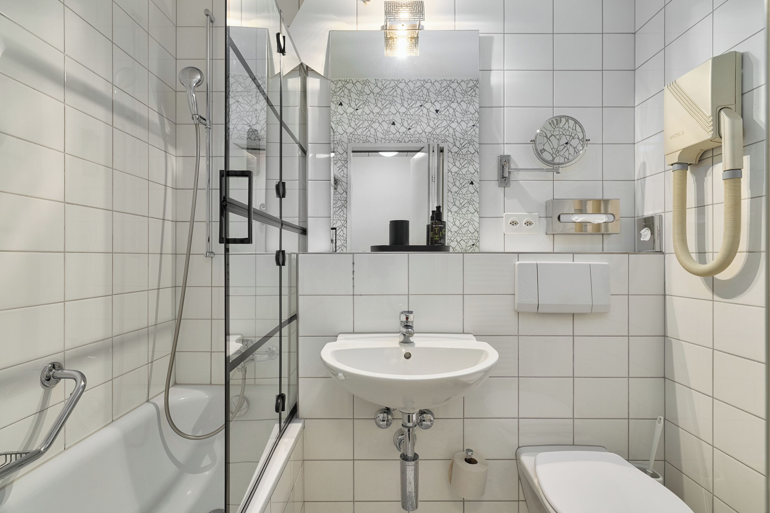 Un baño moderno con bañera, ducha, lavamanos, inodoro y un espejo con un revestimiento de azulejos decorativos.