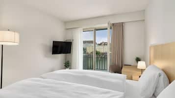 A hotel room with a bed, a TV, a desk, and a view of buildings through the window.