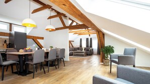 Ein modernes Loft mit freiliegenden Holzbalken, einem Essbereich mit grauen Stühlen, einer Couch und einer Pflanze.