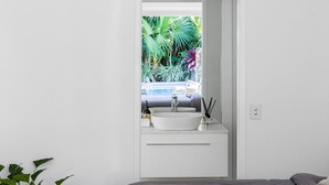 A bathroom with a white sink, a mirror, and a view of a garden with tropical plants.