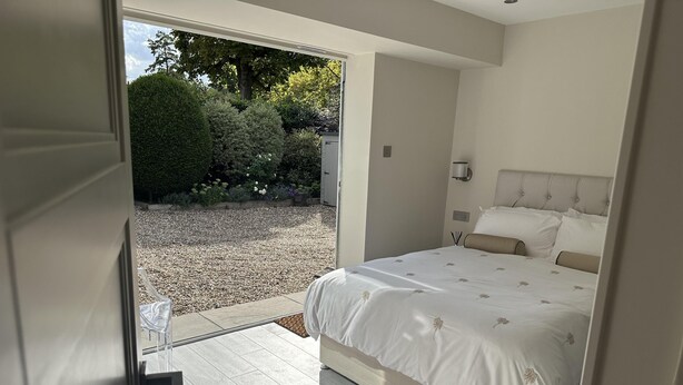 A bedroom with a bed, a door leading to a balcony, and a view of a garden. - Beautiful 1-bed Studio in Bourne end (Bourne End)