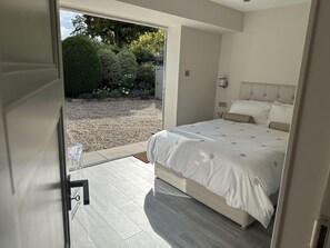 A bedroom with a bed, a door leading to a balcony, and a view of a garden. - Beautiful 1-bed Studio in Bourne end (Bourne End)