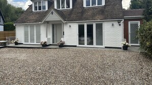 A two-story house with a gravel driveway, a front porch, and a large sliding glass door. - Beautiful 1-bed Studio in Bourne end (Bourne End)