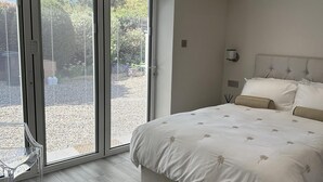 A modern bedroom with a large bed, a glass door leading to an outdoor area, and a clear view of the outside. - Beautiful 1-bed Studio in Bourne end (Bourne End)