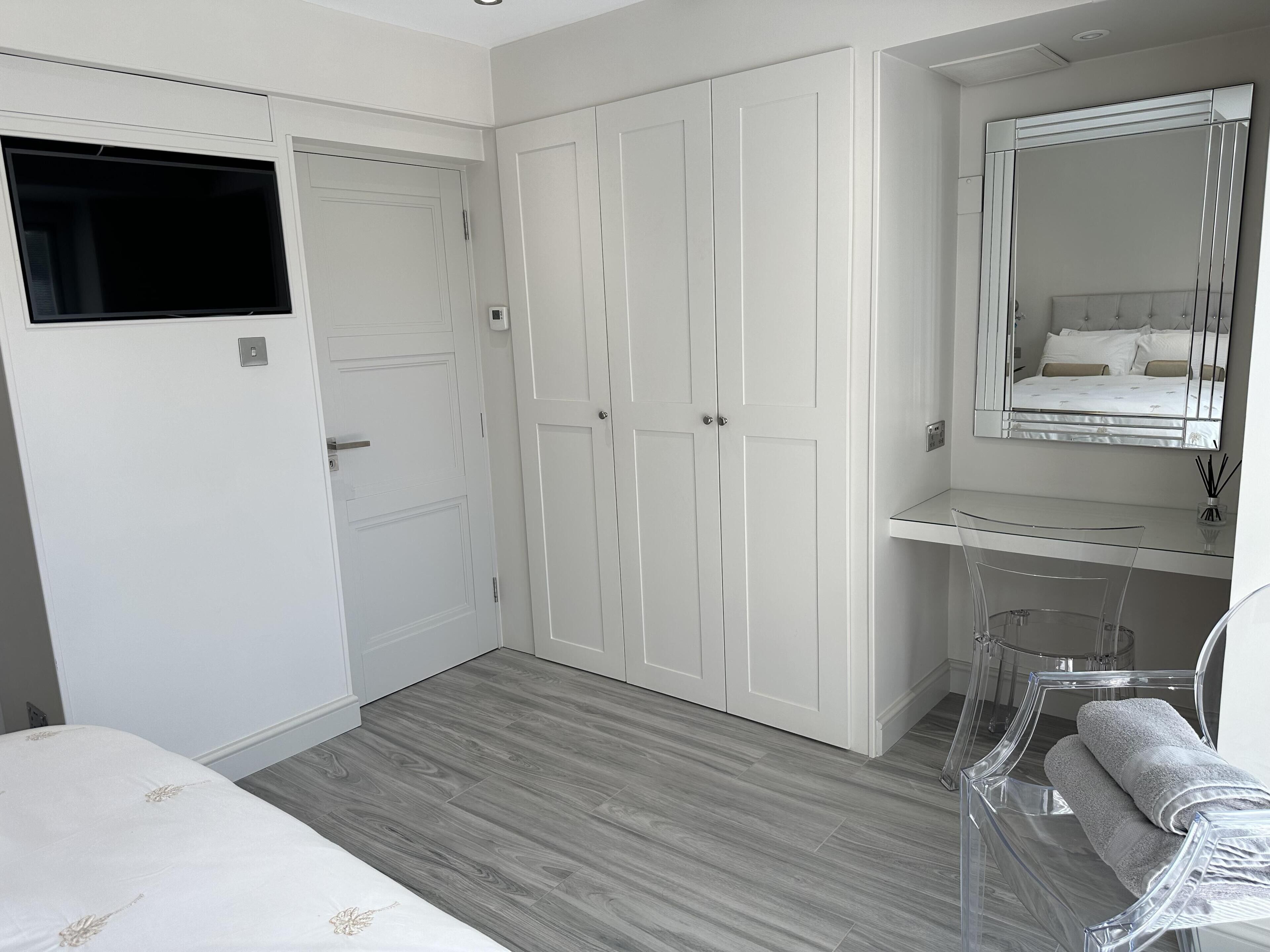 A bedroom with a bed, a wardrobe, a mirror, and a clear chair.