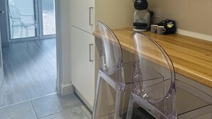 A modern kitchen with a wooden countertop, two clear plastic chairs, and a coffee machine. - Beautiful 1-bed Studio in Bourne end (Bourne End)