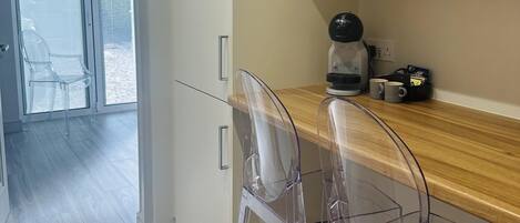 A modern kitchen with a wooden countertop, two clear plastic chairs, and a coffee machine.