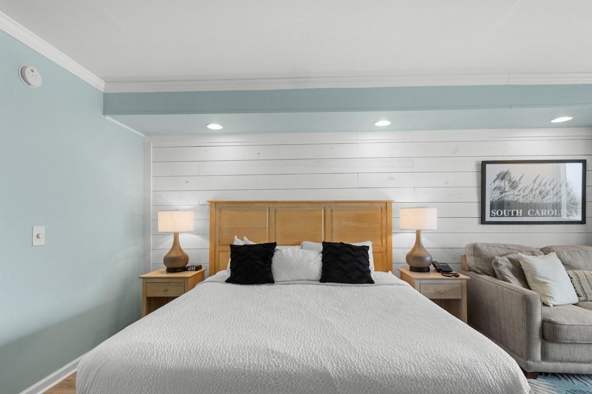 A hotel room with a large bed, two bedside tables with lamps, a sofa, and a framed picture on the wall.
