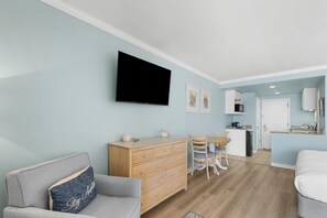 Uma sala de estar com sofá, televisão fixada na parede, aparador de madeira e área de refeições com cadeiras e mesa.