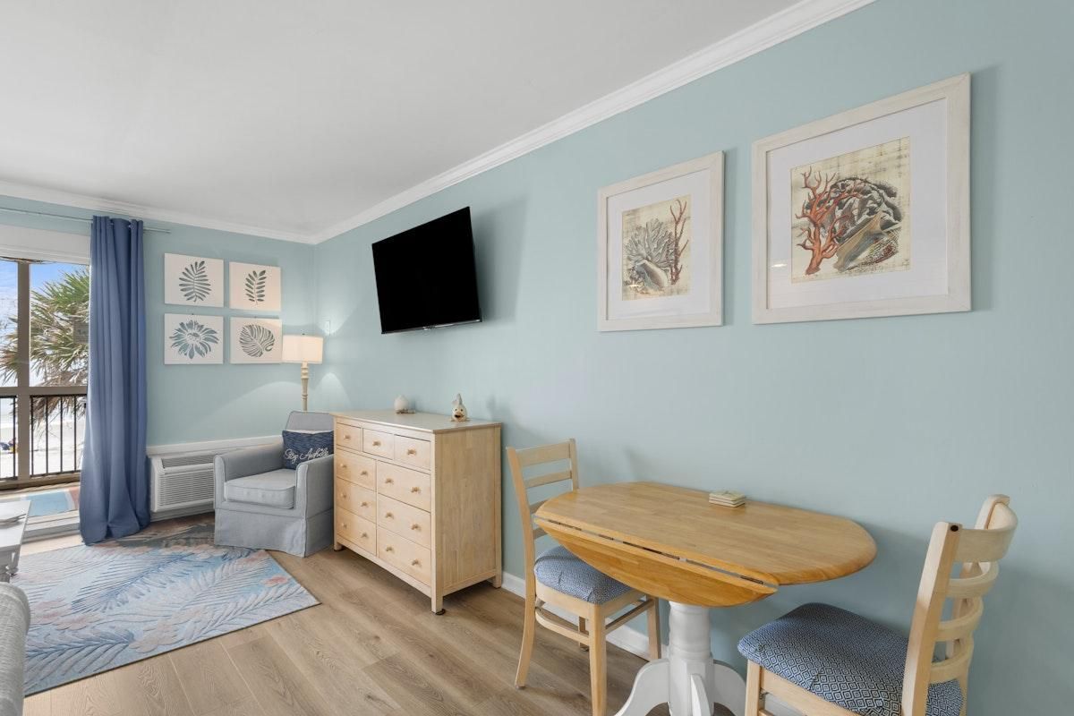Una habitación con una mesa de comedor de madera, dos sillas, un sofá azul, un armario de madera y un televisor de pantalla plana montado en la pared.