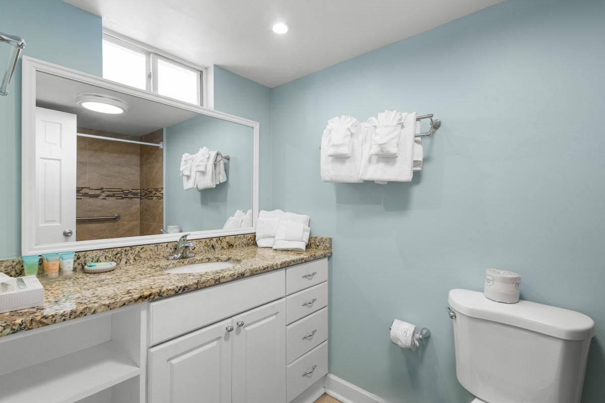 A bathroom with a granite countertop, white cabinets, a toilet, and towels hanging on the wall.