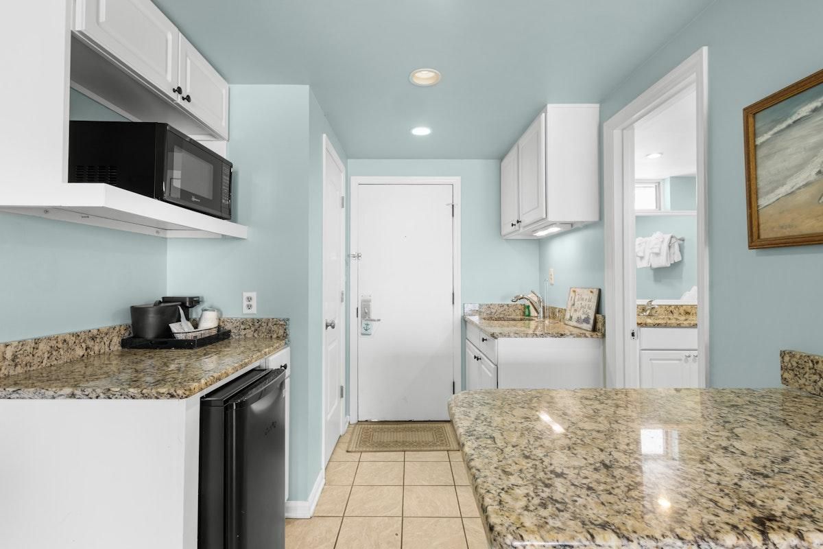 A compact kitchen with white cabinets, a microwave, and granite countertops.