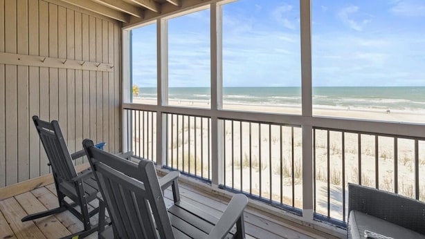 A covered outdoor area with wooden flooring, a railing, and a view of the beach. - Getaway in our Oceanfront Dune Rooms 2nd Floor (Pawleys Island)