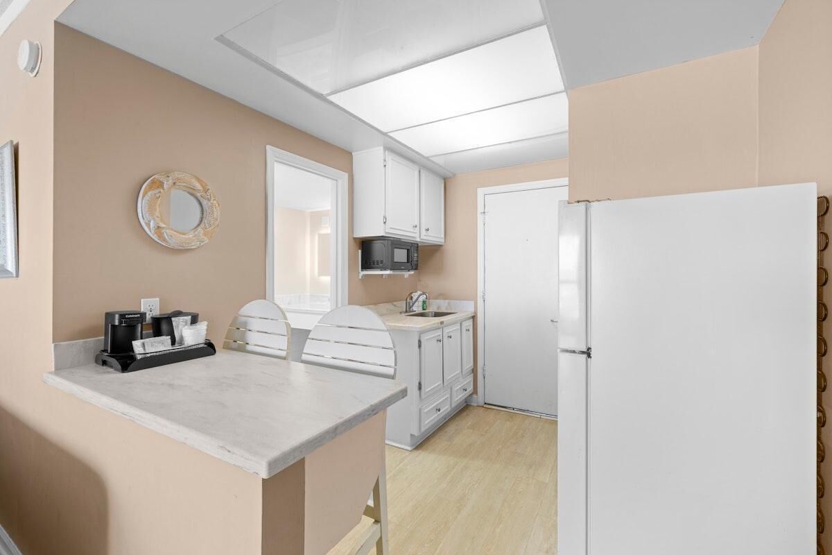 Cocina compacta con armarios blancos, microondas, refrigerador, cafetera y una pequeña isla con asientos.