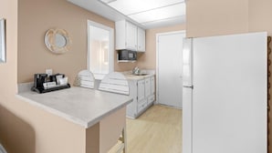 A compact kitchen with white cabinets, a microwave, a refrigerator, a coffee maker, and a small island with seating. - Getaway in our Oceanfront Dune Rooms 2nd Floor (Pawleys Island)