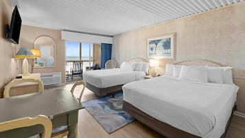 A hotel room with two beds, a dining table, a TV, and a view of the ocean.