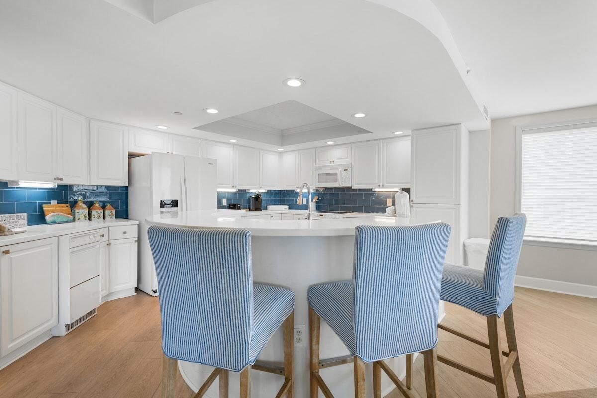 Una cocina moderna con armarios blancos, una isla central con taburetes y un salpicadero de azulejos azules.