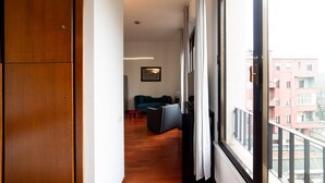 A corridor leading to a living area with a sofa and a small table, a wooden wardrobe, and a window with a view of buildings. - Hbhall Brera 59 (Milan)