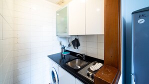 A compact kitchen with white cabinets, a black countertop, a stainless steel sink, a washing machine, and a blue refrigerator. - Hbhall Brera 59 (Milan)