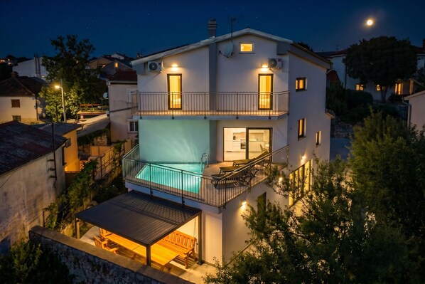 A two-story building with a swimming pool, balconies, and a covered outdoor seating area.